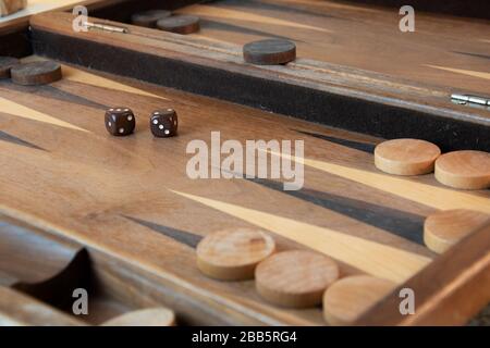 Braune Backgammon-Würfel und -Stücke auf Holzbrett Stockfoto