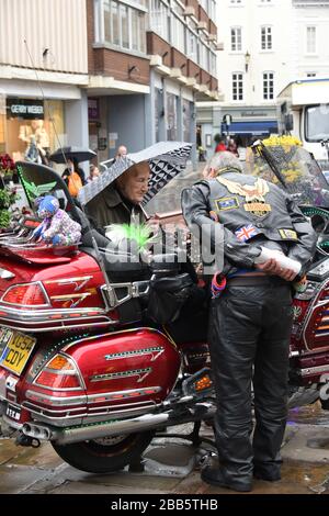 Ältere Frau, die mit einem männlichen Biker spricht, während sie sich ein Motorrad von Honda Goldwing ansieht, das im Regen auf dem Shrewsbury's Town Square geparkt wurde. Stockfoto