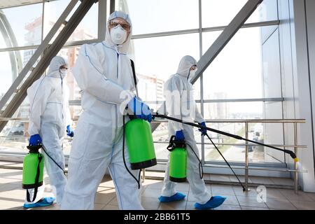 Professionelle Mitarbeiter in hasmat-Anzügen desinfizieren die Unterbringung in Innenräumen Stockfoto