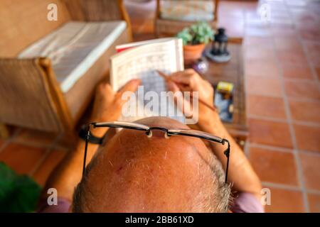 Pensionierter Mann verbringt seine Zeit mit der Lösung von langweiligen Kreuzworträtsel auf der Veranda seines Hauses. Stockfoto