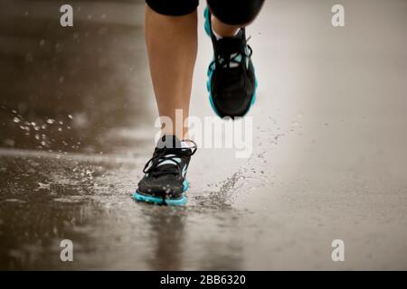 Junge Frau joggen auf einer Straße mit Wohnhäusern im Regen. Stockfoto