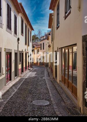 Eine enge, gepflasterte Straße an einem sonnigen Tag im Altstadt-Gebiet von Funchal auf der Insel Madeira, Portugal Stockfoto