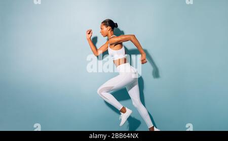 Seitenansicht der jungen Frau beim laufen. Fitnessmodell mit blauem Hintergrund. Stockfoto