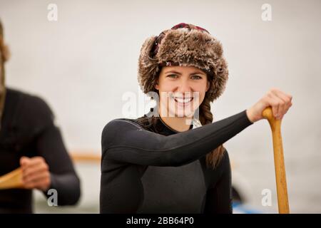 Porträt einer jungen Frau mit einem Pelzhut und Neoprenanzug beim paddeln im Kanu mit Freunden. Stockfoto