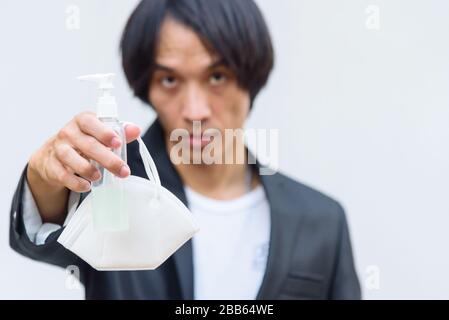 Ein asiatischer Mann zeigt N95-Maske und Alkoholgel zum Schutz vor krankhaften Koviden 19 Stockfoto