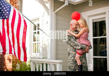 Männliche Soldaten seiner jungen Tochter umarmen auf der Veranda ihres Hauses. Stockfoto