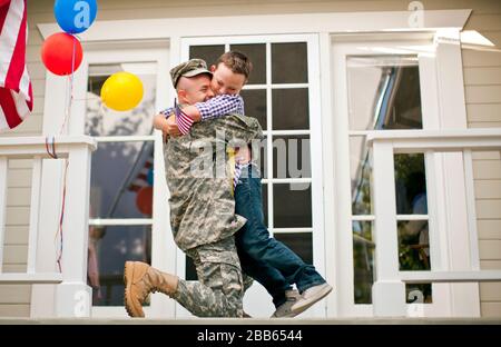 Fröhlicher Armeesoldat umarmte seinen jungen Sohn auf der Vorhalle ihres Hauses. Stockfoto