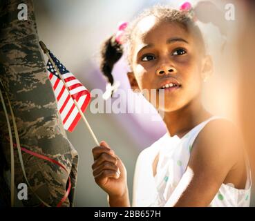 Nachdenkliches junges Mädchen, das eine amerikanische Flagge hält, während es neben jemandem in einer Militäruniform steht. Stockfoto