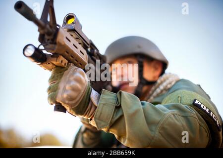 Mitte der erwachsenen Mann in Polizeiuniform Zeigen einer Gewehr. Stockfoto