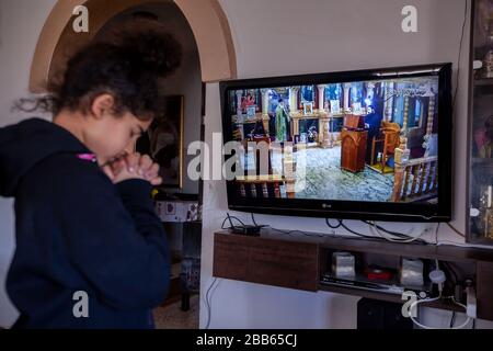 (200330) -- BETHLEHEM, 30. März 2020 (Xinhua) -- EIN palästinensisches Mädchen betet, während sie am 29. März 2020 eine Live-Fernsehübertragung der Sonntagsmesse von einer orthodoxen Kirche in Beit Sahour in der Nähe der Westjordanstadt Bethlehem verfolgt. Zum ersten Mal besuchte Raed al-Atrash, ein 54-jähriger palästinensischer Mann aus der Westjordanstadt Bethlehem, mit seiner Familie die Sonntagsmesse über eine Live-Fernsehübertragung, da die Kirchen im Rahmen der Vorsichtsmaßnahmen gegen die Verbreitung des Romans Coronavirus geschlossen sind.TO GO WITH "Feature: Christen in Palästina besuchen Live-gebeten, während Kirchen in der Nähe von Coronavirus fea stehen Stockfoto
