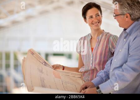 Lächelnde Frau und reifer Mann, die gemeinsam Baupläne betrachten. Stockfoto