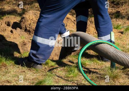 Mann Arbeiter, der Rohr hält und die Reinigung der Kanalisation im Freien bereitstellt. Die Abwasserpumpmaschine verstopft verstopfte Mannlöcher Stockfoto