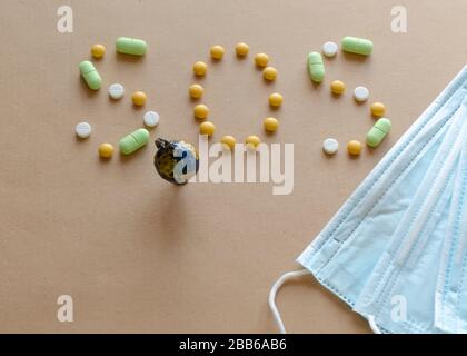 Medizinische Einwegschutzmaske, kleiner Globus und Beschriftung aus den Pillen sos auf hellem Hintergrund. Coronavirus Konzept Stockfoto