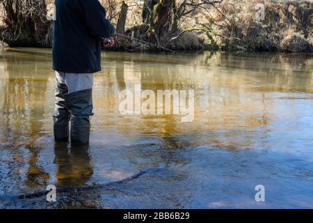 Fischer mit Gummistiefeln Forellenfischen an einem sonnigen Tag in einem Bach. Angler, der künstliche Köder in einem Fluss wirft Stockfoto