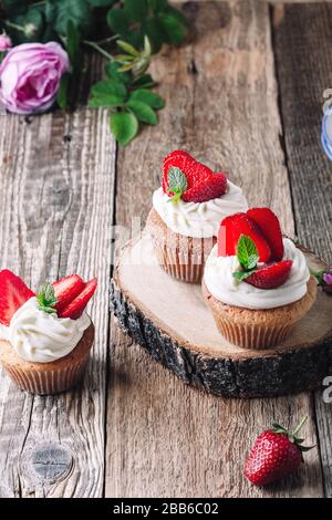 Hausgemachte Cupcakes mit Erdbeeren und Sahne auf rustikalem Holztisch in der Nähe, Sommerdessert Stockfoto