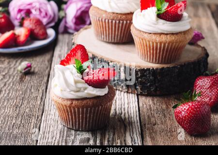 Hausgemachte Cupcakes mit Erdbeeren und Sahne auf rustikalem Holztisch in der Nähe, Sommerdessert Stockfoto