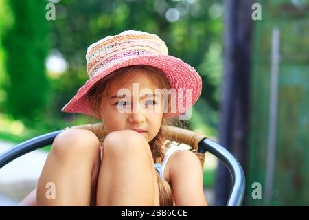 Portrait des süßen traurigen kleinen Mädchens auf dem großen Hut, das am Sommertag traurig aussieht Stockfoto