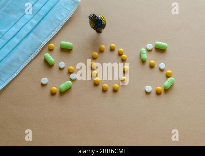 Medizinische Einwegschutzmaske, kleiner Globus und Beschriftung aus den Pillen sos auf hellem Hintergrund. Coronavirus Konzept Stockfoto