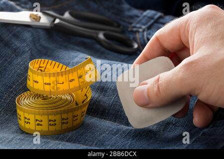 Mann Markierlinie mit Schneiderkreide auf Jeans Denim-Material mit Schere und Maßband auf blauen Jeans Denim Nahaufnahme - Jeans Mode bedrohend oder re Stockfoto