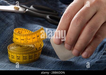 Mann Markierlinie mit Schneiderkreide auf Jeans Denim-Material mit Schere und Maßband auf blauen Jeans Denim Nahaufnahme - Jeans Mode bedrohend oder re Stockfoto