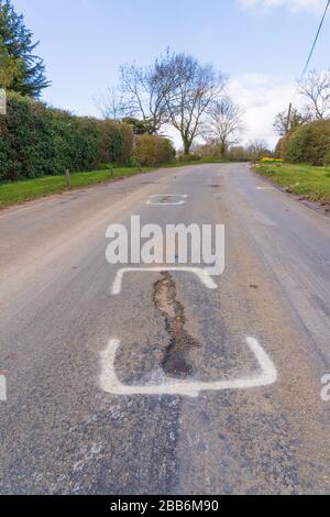 Weiße, mit Sprühfarbe lackierte Markierungen, die von Fremdfirmen für zukünftige Straßenbauarbeiten auf der Straße hinterlassen wurden. Perry Green, Much Hadham, Hertfordshire. GROSSBRITANNIEN Stockfoto