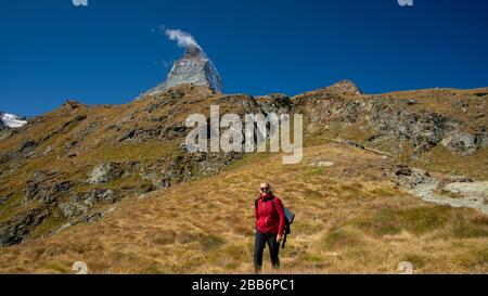 Lächelnde Frau, die in den Bergen mit Matterhorn-Gipfel in der Ferne, Zermatt, Schweiz, wandert Stockfoto