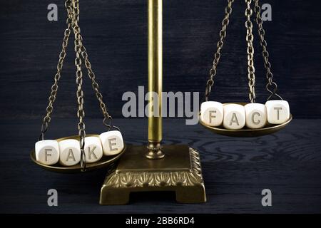 Gefälschtes Nachrichtenkonzept. Maßstab mit Holzwürfeln gefälscht und Fakt auf dunklem Holzhintergrund. Stockfoto
