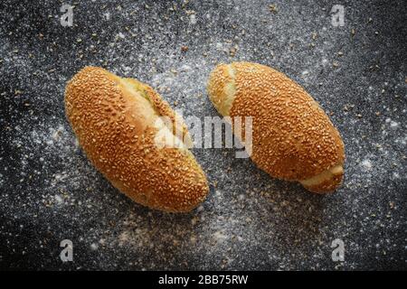 Flacher Laienschuss von frischen fwo-Maisbrötchen mit Sesamsamen auf schwarz bestreut mit Mehl und Sesamsamen Backgroud Stockfoto