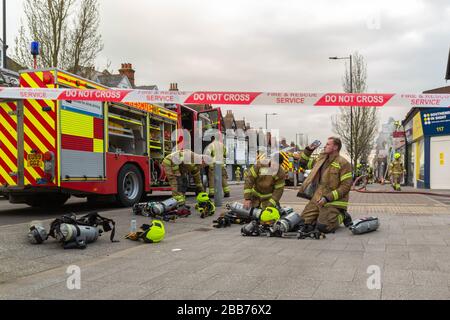 Southend-on-Sea, Großbritannien. 30. März 2020. Feuerwehrleute des Essex Fire and Rescue Service machen nach einem Brand in der Hamlet Court Road in Westcliff-on-Sea eine Pause. Neben dem Feuerwehrfahrzeug befinden sich Atemgeräte und Helme mit Trinkwasser eines Feuerwehrmannes. Der Tatort ist mit einem rot-weißen Band „FEUERWEHR und RETTUNGSDIENST“ abgesperrt, das die Nachwirkungen der Notfallmaßnahmen unterstreicht. Penelope Barritt/Alamy Live News Stockfoto