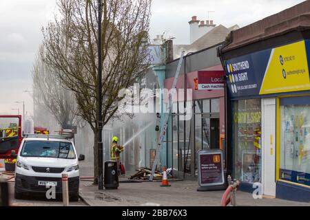 Southend-on-Sea, Großbritannien. 30. März 2020. Die Besatzungen der Essex Fire Brigade bekämpfen ein Ladenfeuer auf der Hamlet Court Road in Westcliff-on-Sea. Aus dem betroffenen Gelände bläst Rauch auf, wenn die Feuerwehr Wasser auf das Gebäude sprühen kann. Rettungsfahrzeuge und Trümmer sind auf der Straße zu sehen, mit angrenzenden Unternehmen wie Southend Vision Sight und lokalen Geldautomaten. Der Vorfall führte zu einer raschen Reaktion der öffentlichen Sicherheit. Penelope Barritt/Alamy Live News Stockfoto
