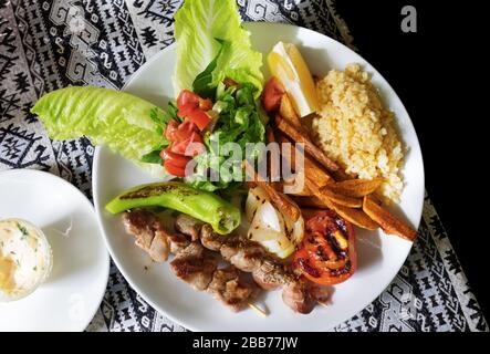 Traditionelles türkisches Mittagessen. Gegrilltes Lammkebab auf Holzspießen mit Beilage und Zitronenscheibe auf dem Tisch mit Tischdecke. Ansicht von oben. Stockfoto