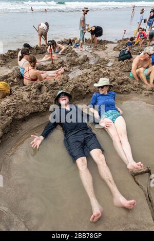 Touristen, die sich in heißen Pools entspannen, die im Sand gegraben wurden, Hot Water Beach, in der Nähe von Hahei, North Island, Neuseeland Stockfoto