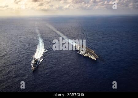 Der Flugzeugträger der Nimitz-Klasse der US-Marine USS Theodore Roosevelt in Formation mit dem Lenkflugkörperzerstörer der Arleigh-Burke-Klasse USS Bunker Hill, während sie einen routinemäßigen Transit am 18. März 2020 in der philippinischen See durchführen. Stockfoto