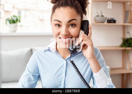 Der Reiseleiter sitzt am Tisch im Büro und hält das Telefon und spricht mit der Kamera, die den Kunden anschaut Stockfoto
