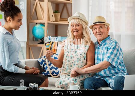 Reisebüro im Büro mit älteren Kunden in Strandhüten fröhlich halten Pässe und Flugtickets Stockfoto