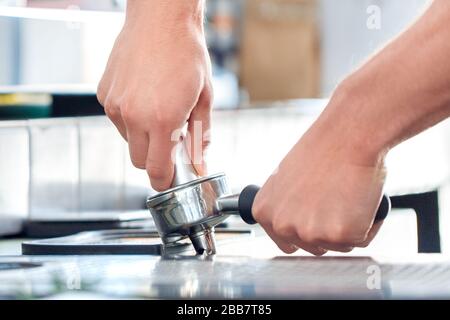 Kaffeelaffee. Der junge Barista im Café hält einen Portafilter, der Kaffee aus nächster Nähe eintampft Stockfoto
