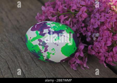 Osterhintergrund. Kunst bemaltes Ei mit Flieder auf Holzhintergrund. Stockfoto