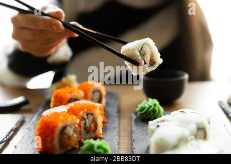 Schöne junge Frau, die Sushi-Rolle im Café isst. Frau, die Sushi mit Essstäbchen im Restaurant isst. Stockfoto
