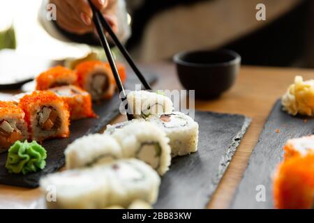 Schöne junge Frau, die Sushi-Rolle im Café isst. Frau, die Sushi mit Essstäbchen im Restaurant isst. Stockfoto