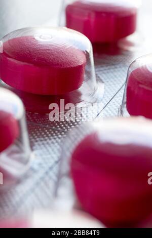 Pillen in Blister. Makro-Nahaufnahme der roten medizinischen Pillen in Blisterpackungsstreifen auf grauem Hintergrund für die Verwendung als medizinischer oder pharmazeutischer Hintergrund. Stockfoto