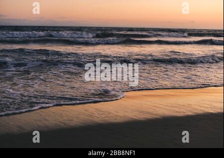 Die Ozeanwellen in der Dämmerung mit Blick auf den Sand und den roten Himmel - Natur - Pazifik Stockfoto