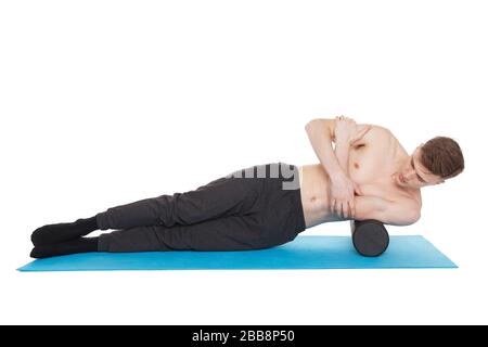 Der gutaussehende Mann zeigt Übungen mit einer Schaumstoffrolle für eine Myofaszialmassage auf der Trainingsmatte im Studio. Isoliert auf weiß. Stockfoto