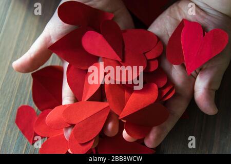 Rote Herzen aus Papier in Childhänden. Ein Geschenk für Valentinstag und Muttertag. Stockfoto