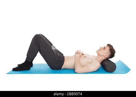 Der gutaussehende Mann zeigt Übungen mit einer Schaumstoffrolle für eine Myofaszialmassage auf der Trainingsmatte im Studio. Isoliert auf weiß. Stockfoto