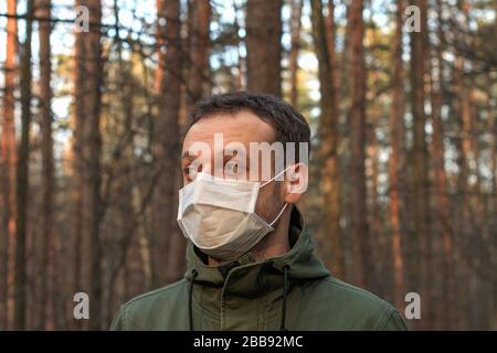 Ein Mann auf einem Spaziergang in einem Wald, der während einer Quarantäne am Abend eine weiße chirurgische Gesichtsmaske trägt Stockfoto