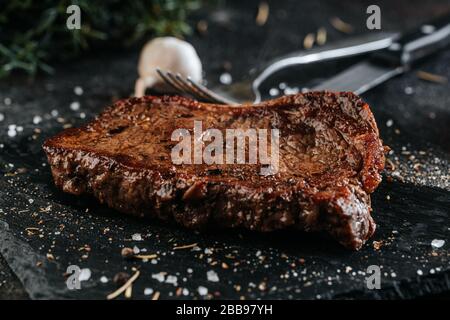Gegrilltes Sirloin-Steak auf der schwarzen Marmorplatte, gewürzt mit Gewürzen Stockfoto
