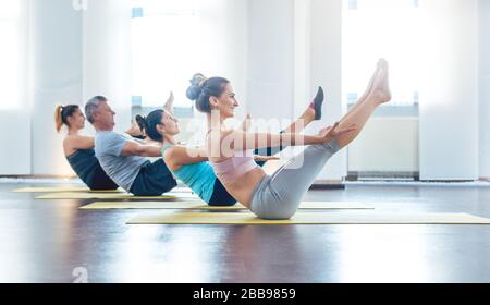 Frauen und Männer, die eine Yoga-Klasse haben, die das Boot posieren Stockfoto