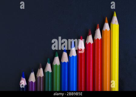 Farbige Bleistifte, die in einer Erhöhung auf dunklem Hintergrund ausgekleidet sind Stockfoto
