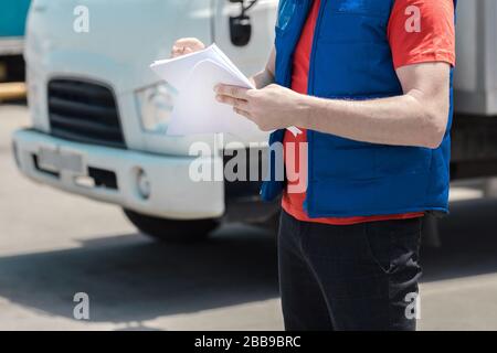 Kurierfahrer in Uniform macht Notizen in Dokument und Lieferung weißer LKW behinde ihn Stockfoto
