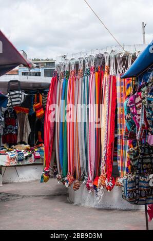 OTAVALO, ECUADOR - 28. JULI 2018: Ein Straßenhändler, der ein Sortiment an wunderschönem Stoff verkauft. Stockfoto